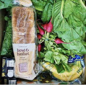 A box of food containing for example bread, bananas, radishes, and salad.