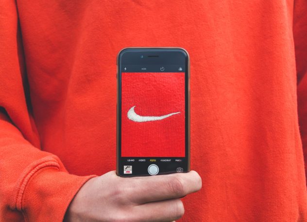 Photograph of person in red sweatshirt holding iphone with red image of Nike tick