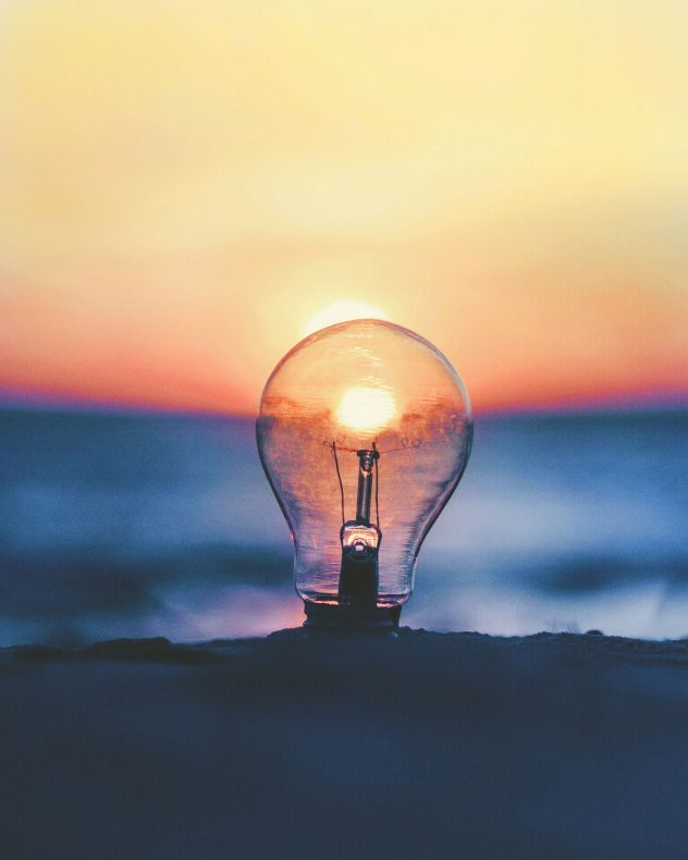 Photograph of lightbulb on beach against a sunset.