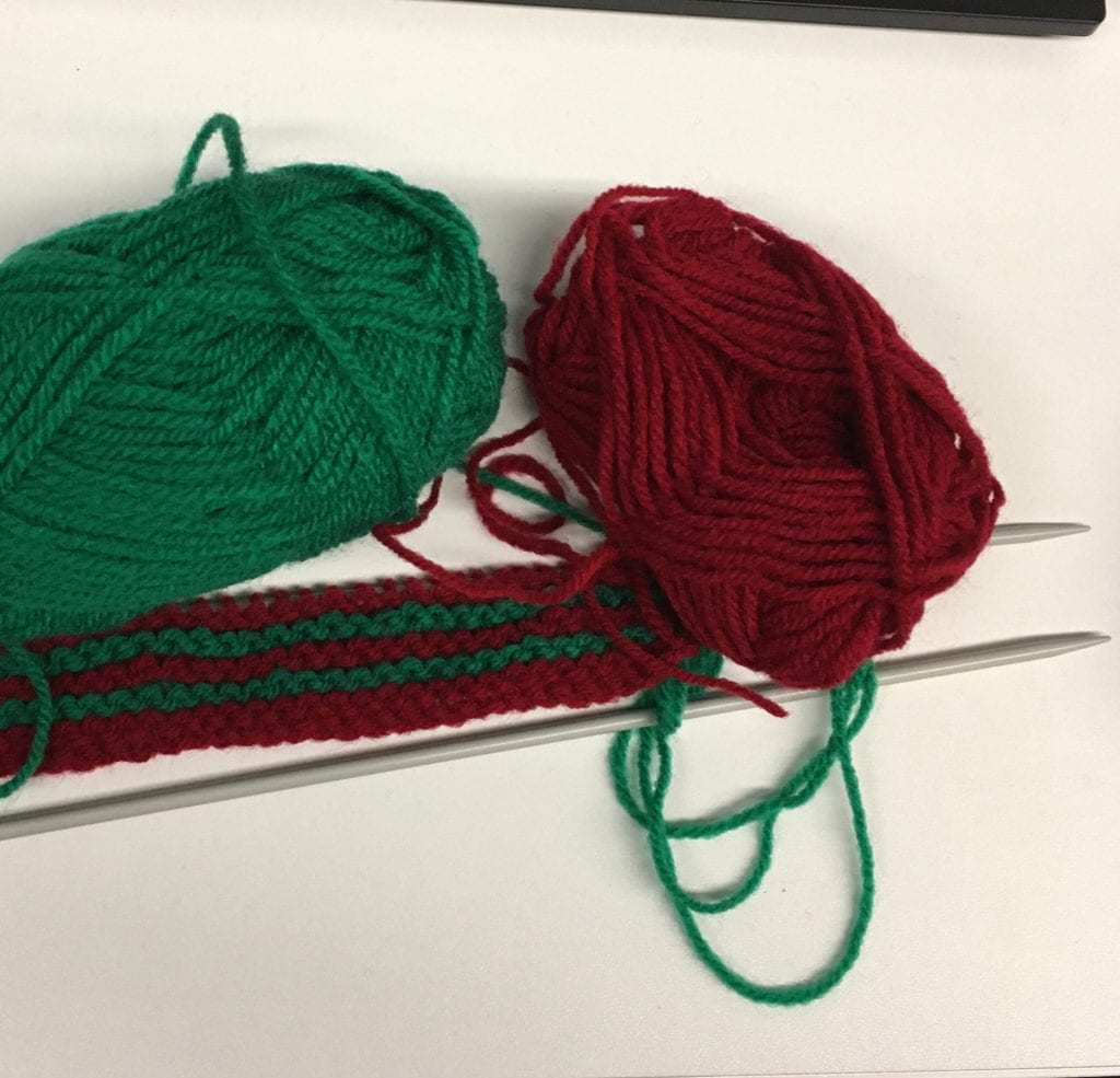 A short piece of knitting, two needles. Balls of red and green wool