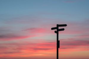 A silhouette of a signpost pointing in different directions against a sunset sky
