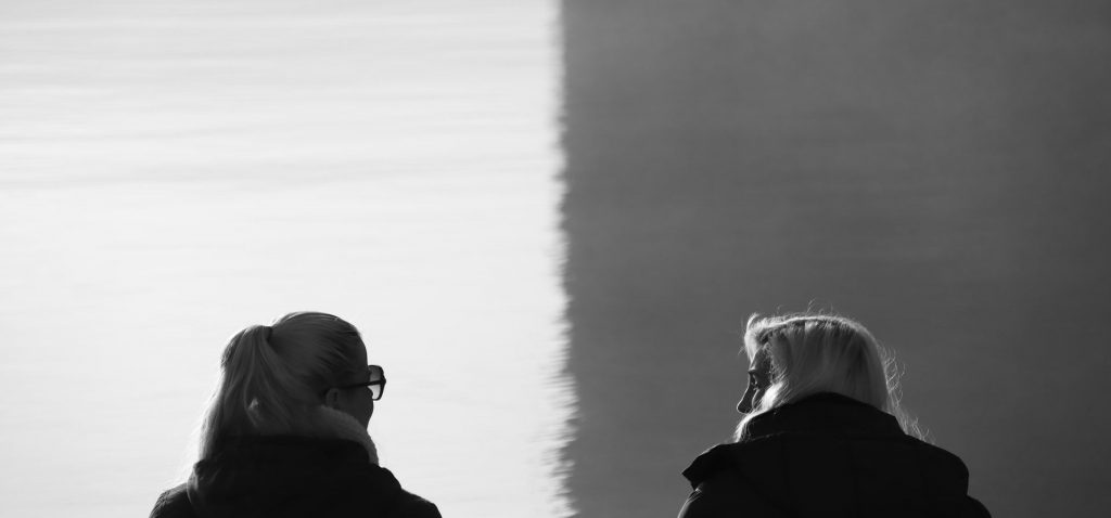 black and white photo of two people looking at each other, backs towards the viewer