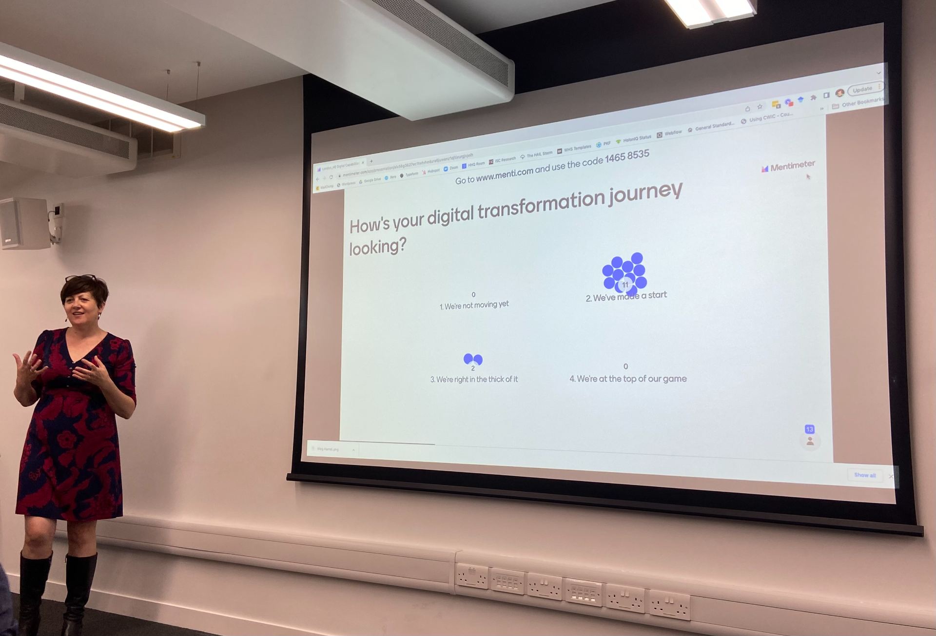 Maria Spies from HolonIQ standing to the left of a screen displaying a poll about where participants are on their digital transformation journey. The poll indicates that the majority have just started, with a small number 'in the thick of it'.