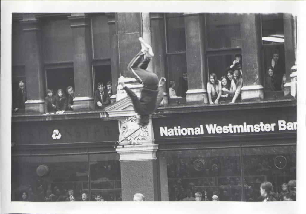 A person in a tracksuit somersaulting with National Westminster Bank in the background.