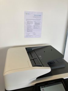 Poster displayed above a printer/copier device (MFD).
