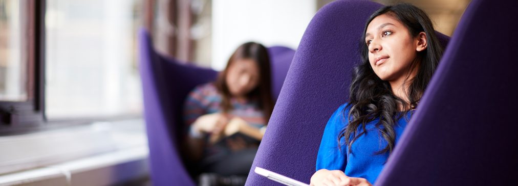 A student sitting on one of the Level 2 purple wingback chairs wistfully enjoying a book.