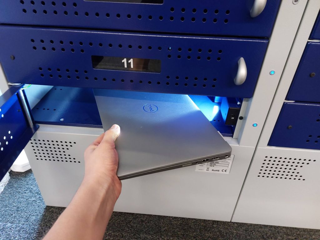A hand reaching for a laptop and removing it from a cabinet.