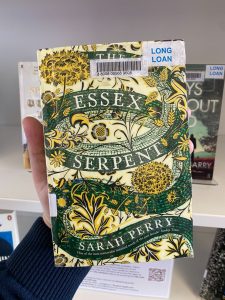 A hand is holding a print copy of 'The Essex Serpent,' by Sarah Perry