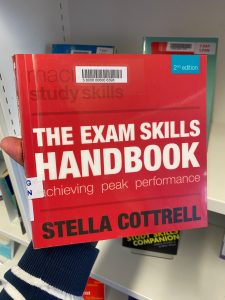 A hand is holding a print copy of The Exam Skills Handbook by Stella Cotrell