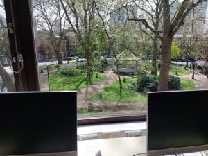 Two PCs with green and leafy Northampton Square visible in the background through a window